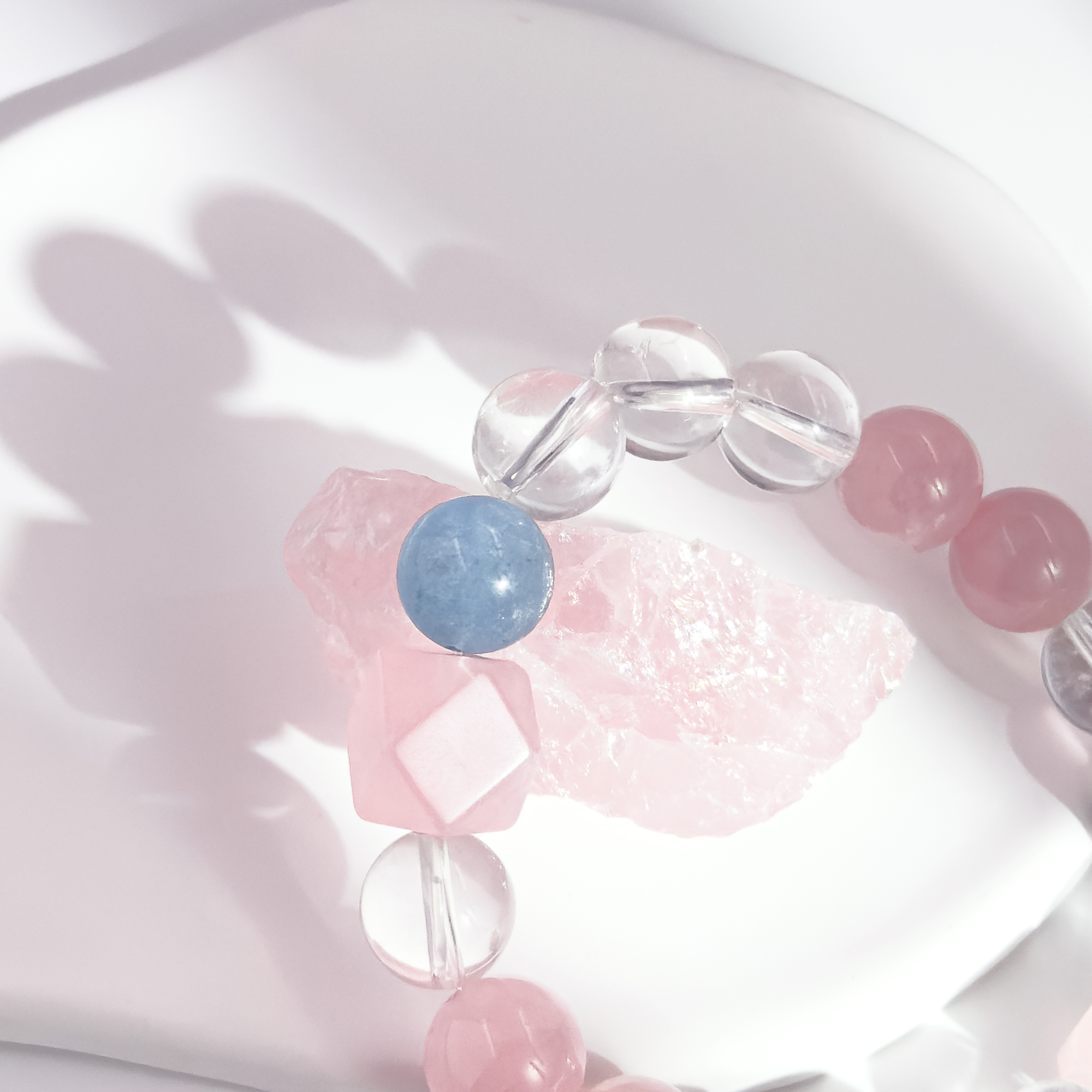 Close-up detail of the rose quartz and clear crystal bracelet showing the mist-blue accent bead resting on a raw rose quartz stone