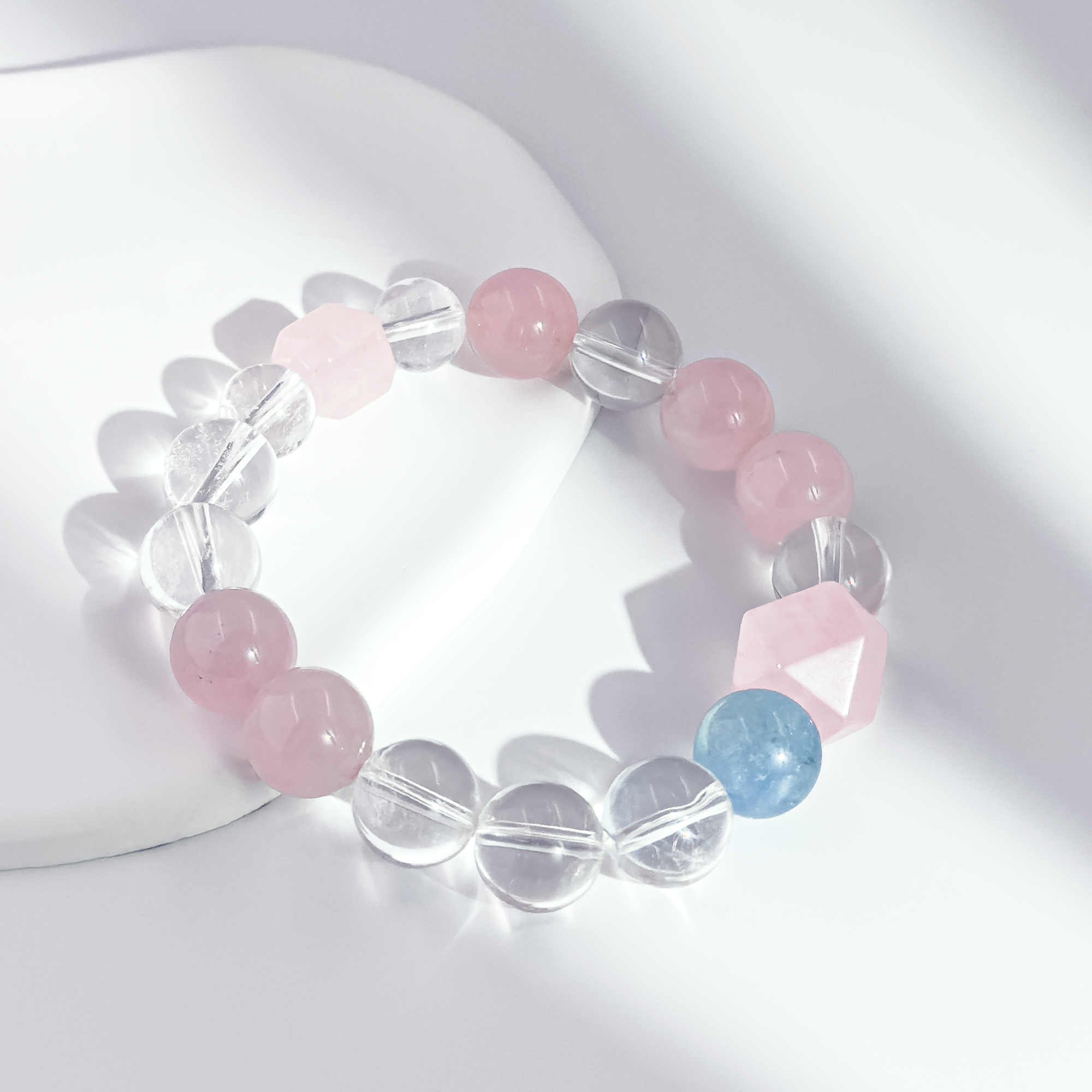 Rose quartz and clear crystal bracelet photographed on a soft white ceramic surface under diffused light